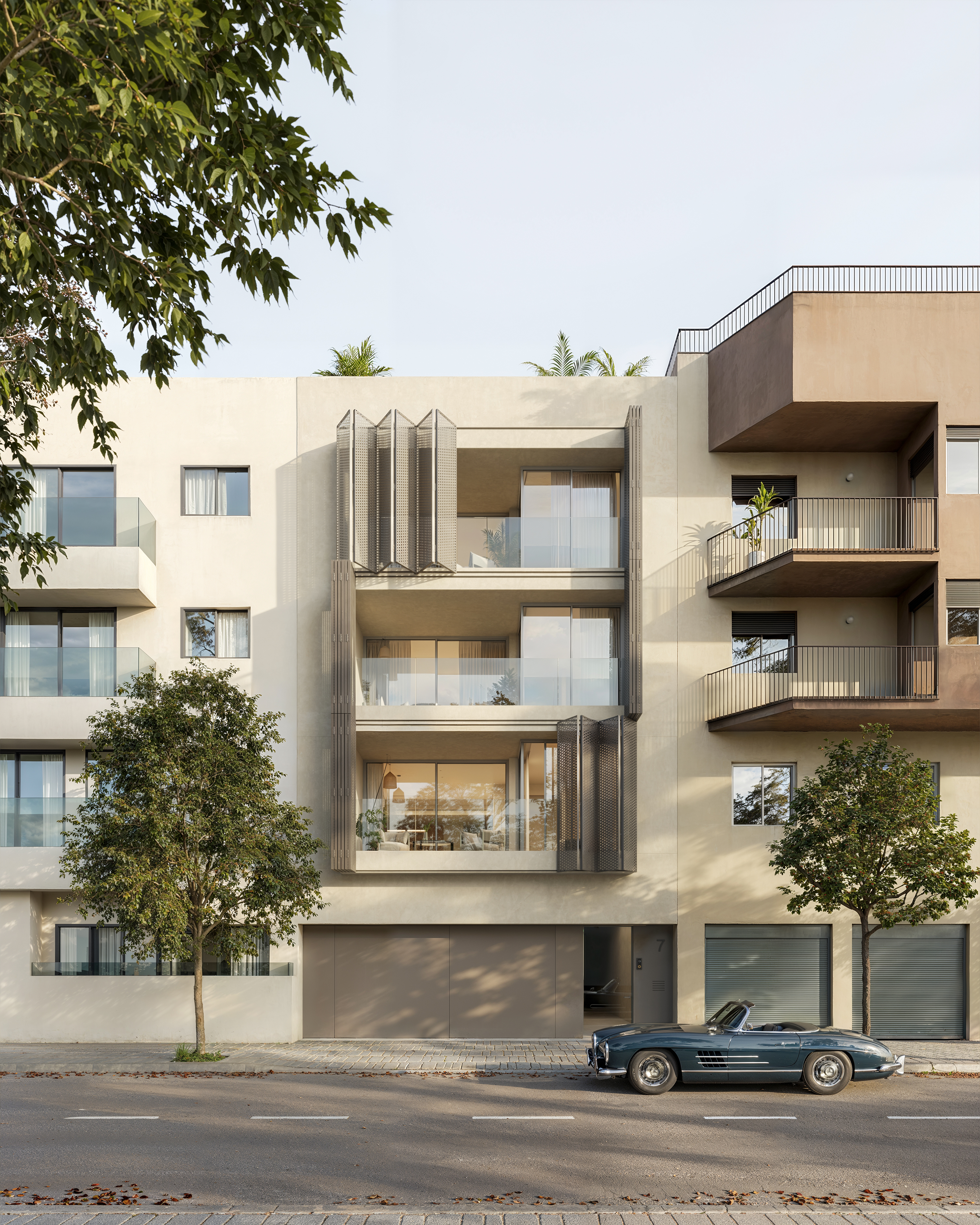 Façana principal d'un edifici plurifamiliar modern a Girona amb els porticons metàl·lics oberts, deixant veure els balcons i l'interior lluminós dels habitatges. A peu de carrer hi ha un cotxe clàssic blau aparcat davant la planta baixa.