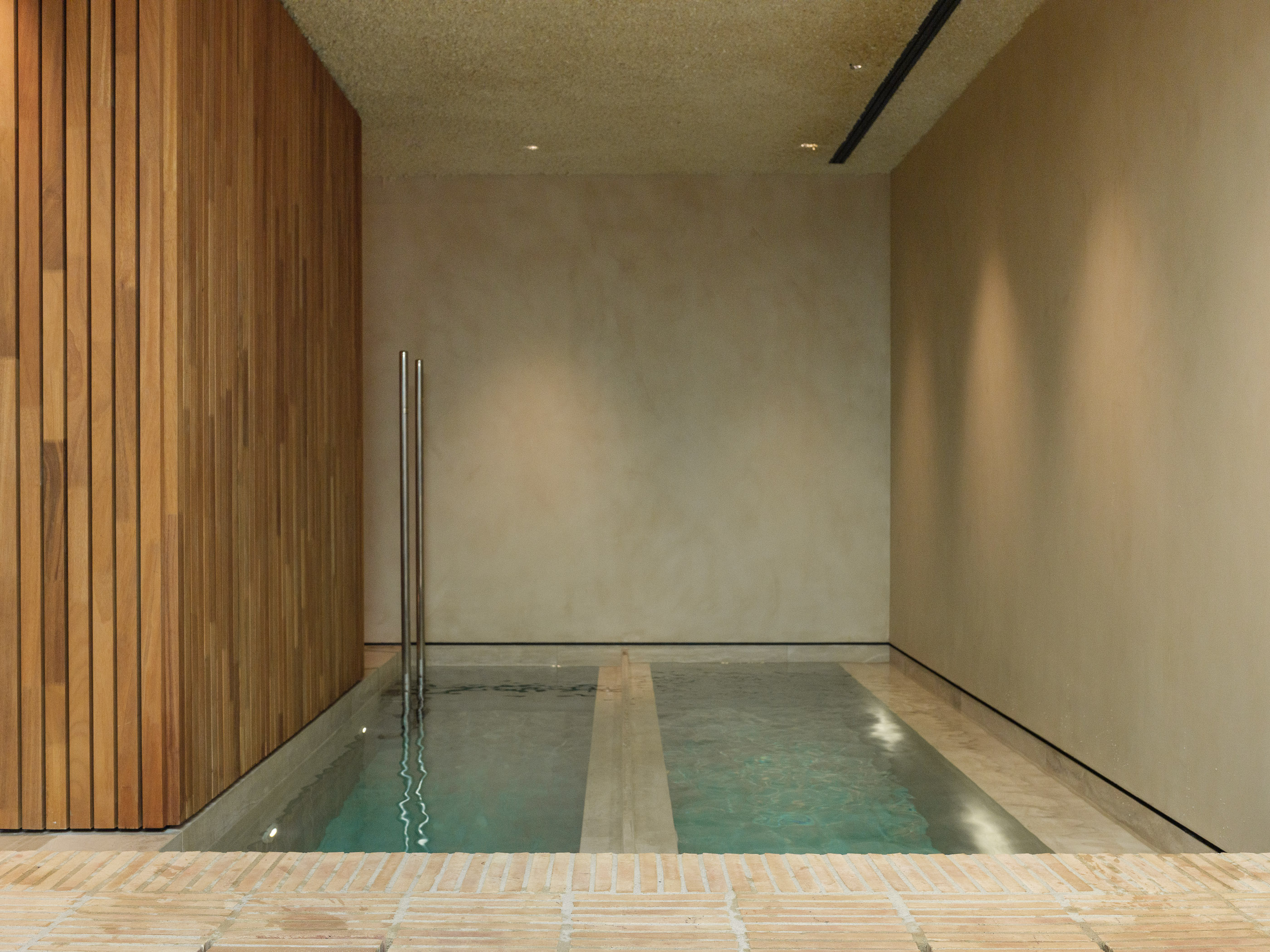 Interior d'un SPA d'hotel reformat al Maresme per a [Nom del teu Despatx]. Disseny arquitectònic minimalista amb llum zenital, tons càlids i materials naturals per a la zona d'aigües.